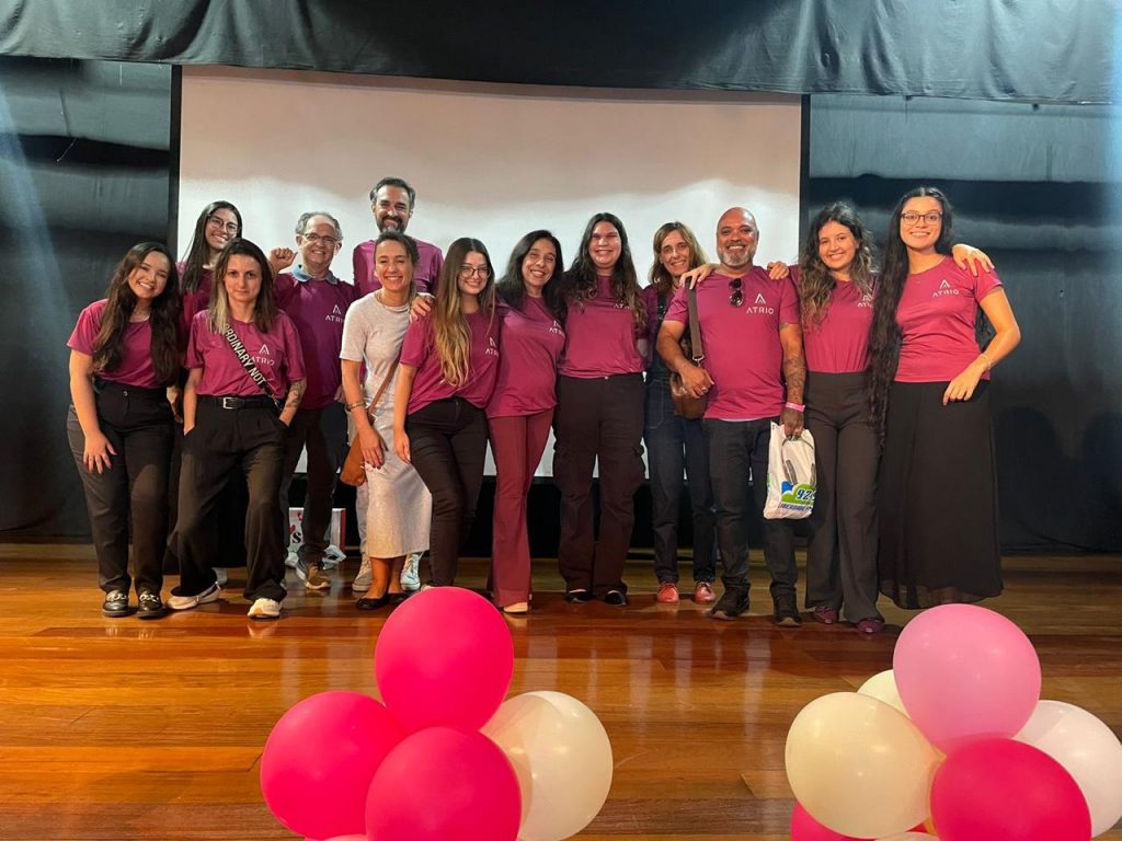 Integrantes da Agência Atrio e professores da Universidade Fumec em um palco, posando para uma foto. Balões cor-de-rosa decoram o ambiente. 